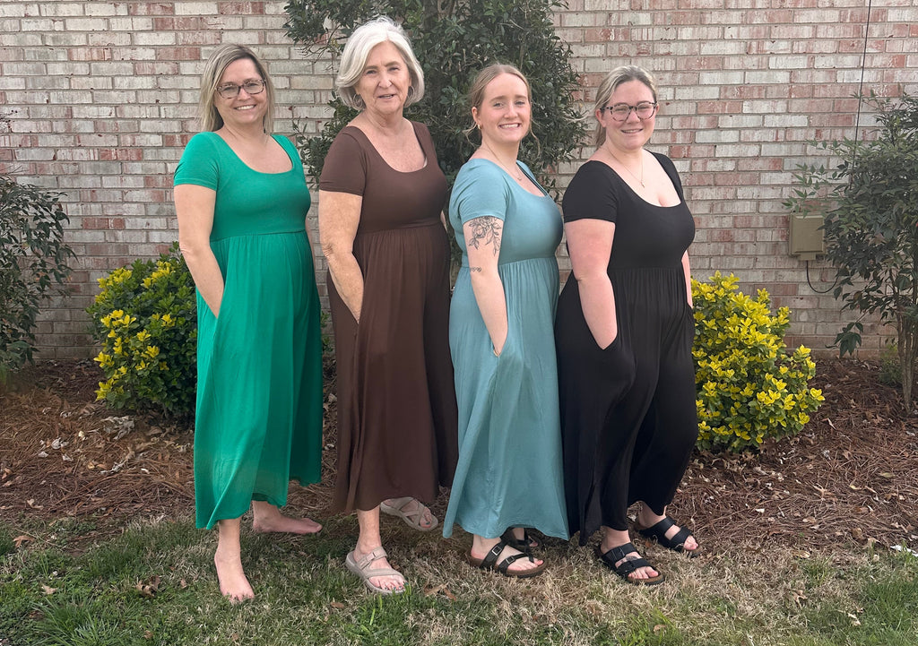 Four women standing outdoors on a grassy area with a building in the background